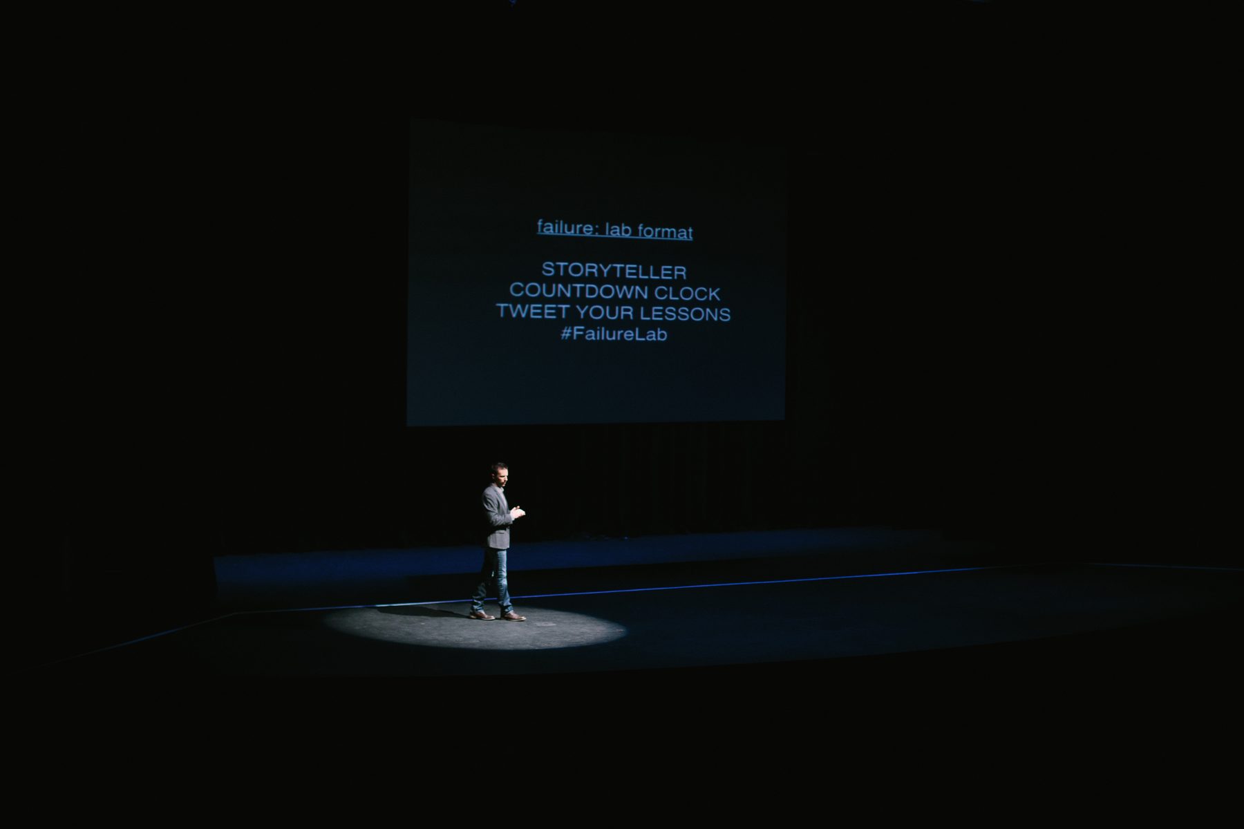 Mike Mudrey hosting Failure:Lab Atlanta, alone in a spotlight on a darkened stage before a full theater